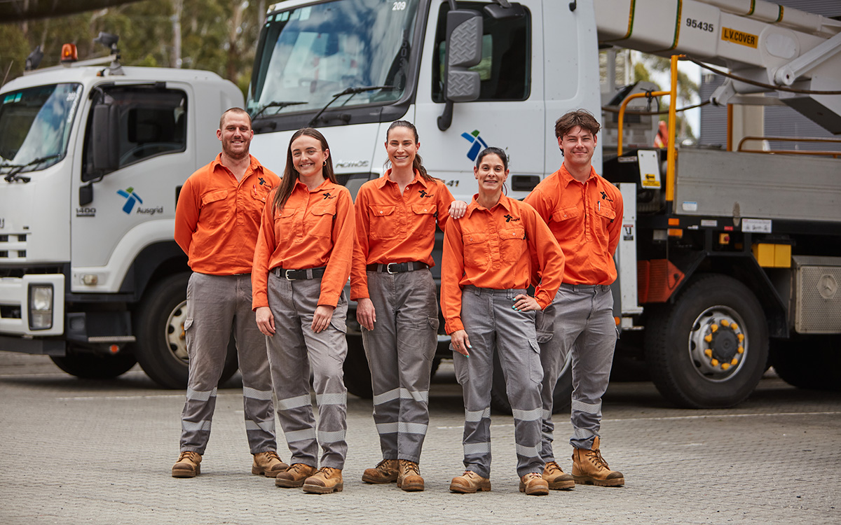 Five field workers (male and female) in orange and grey uniforms in front of Ausgrid truck