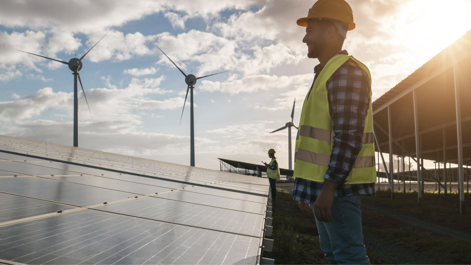 Engineer staring over solar panels, wind mills in background