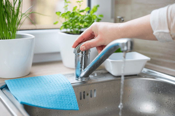 Person with hand on tap in kitchen with water running out of tap 
